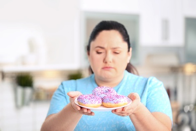 Photo of Sad overweight woman with donuts in kitchen. Failed diet