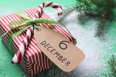 Gift box, paper tag with date 6th of December, fir tree branch on green background, closeup. Saint Nicholas Day