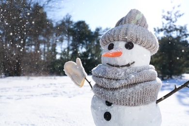 Funny snowman with hat and scarf in winter forest on sunny day, closeup. Space for text