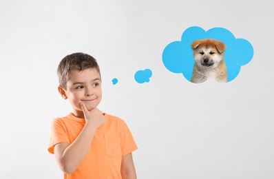 Little boy on light background dreaming about cute puppy