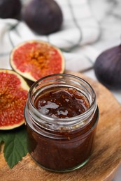 Glass jar of tasty sweet fig jam and fruits on table