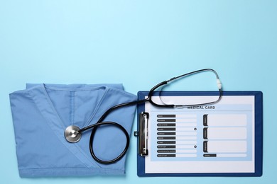 Photo of Medical uniform, stethoscope and clipboard on light blue background, flat lay. Space for text