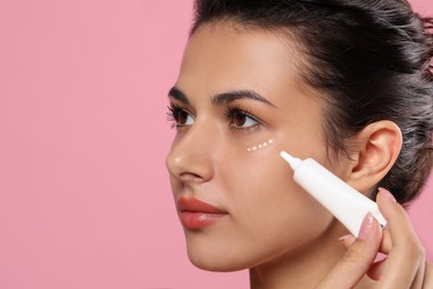 Woman applying cream under eyes on pink background, closeup. Skin care, space for text