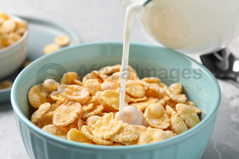 Pouring milk into bowl with cornflakes on table, closeup
