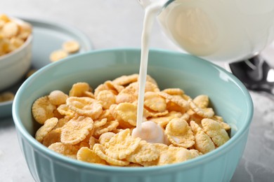 Pouring milk into bowl with cornflakes on table, closeup