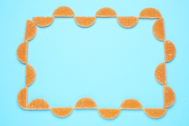 Frame made with orange marmalade candies on light blue background, flat lay. Space for text