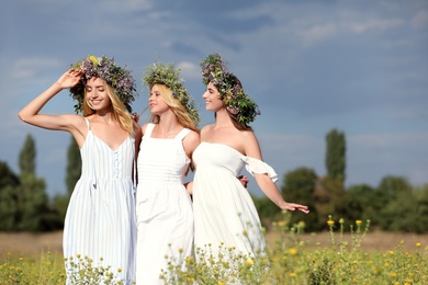 Young women wearing wreaths made of beautiful flowers in field on cloudy day