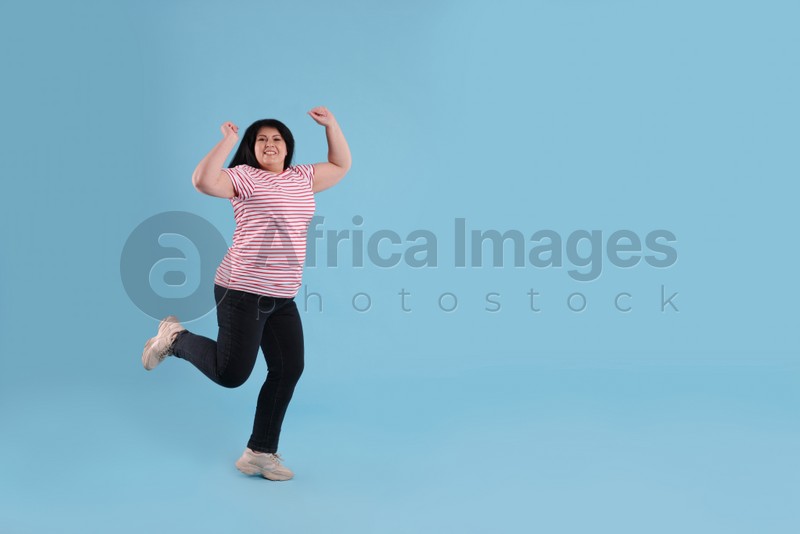 Beautiful overweight mature woman jumping on turquoise background. Space for text