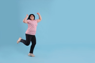 Beautiful overweight mature woman jumping on turquoise background. Space for text