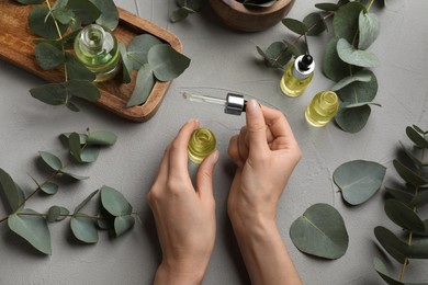 Woman taking eucalyptus essential oil with dropper from bottle at grey table, top view