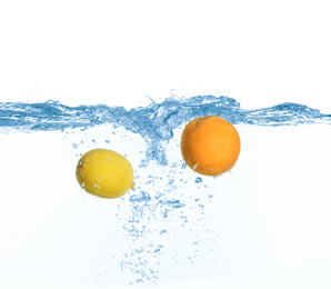 Ripe orange and lemon falling down into clear water with splashes against white background