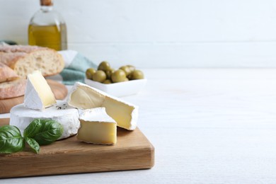 Tasty brie cheese with basil on white wooden table, space for text