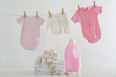 Fresh baby laundry hanging on clothesline and bottle of detergent on white background