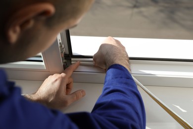 Photo of Construction worker putting sealing foam tape on window indoors, closeup