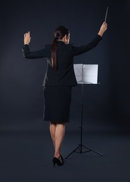 Professional conductor with baton and note stand on dark background, back view