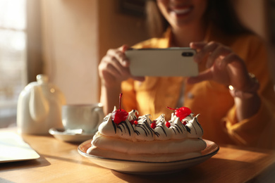 Young blogger taking picture of dessert at table in cafe, focus on plate