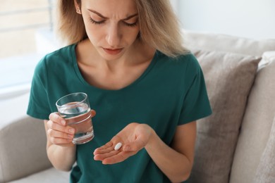 Upset young woman with abortion pill and glass of water at home, closeup