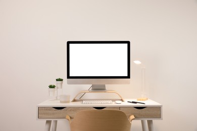 Comfortable workplace with blank computer display on desk near light wall. Space for text