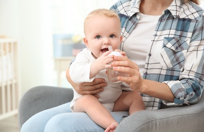 Lovely mother giving her baby drink from bottle in room