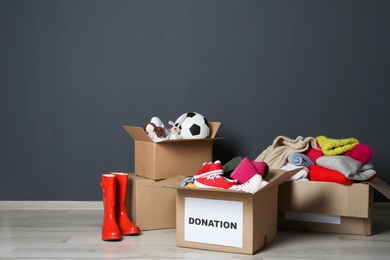 Carton boxes with donations on floor near grey wall. Space for text