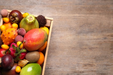 Crate with different exotic fruits on wooden table, top view. Space for text