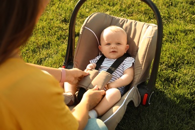 Mother fastening baby to child safety seat outdoors