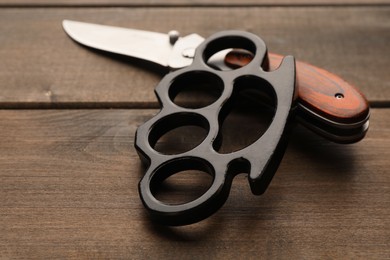 Black brass knuckles and knife on wooden background, closeup