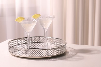 Photo of Tray with martini glasses of fresh cocktail and lemon slices on white table indoors. Space for text