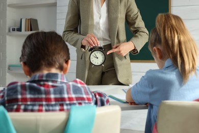 Teacher scolding pupils for being late in classroom, focus on alarm clock