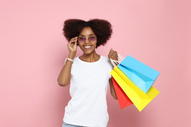 Photo of Happy African American woman in glasses with shopping bags on pink background