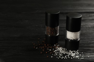 Photo of Salt and pepper shakers on black wooden table, closeup. Space for text