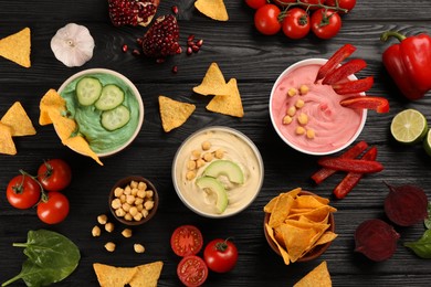 Different kinds of tasty hummus served with nachos on black wooden table, flat lay