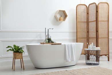 Modern ceramic bathtub and green plants near white wall in room