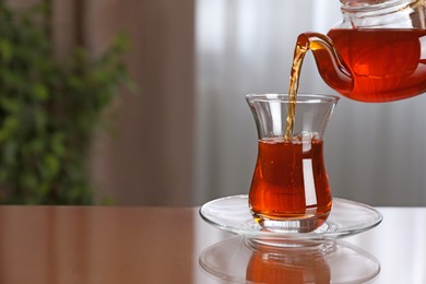 Photo of Pouring tasty Turkish tea into glass on brown table indoors, space for text