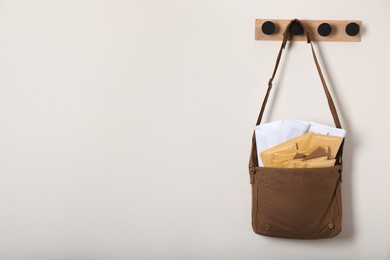 Brown postman bag with newspapers and mails hanging on light wall, space for text