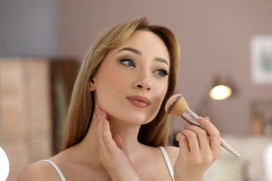 Reflection of beautiful young woman applying face powder with brush in mirror at home