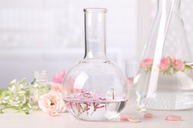 Flask with rosebay flowers on white wooden table. Essential oil extraction