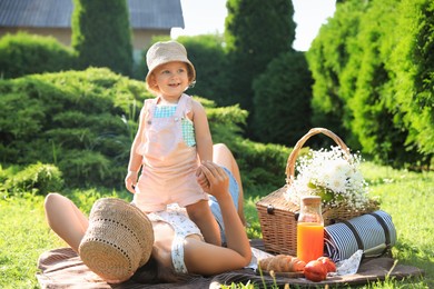 Photo of Mother with her baby daughter resting while having picnic in garden on sunny day