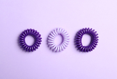 Stylish spiral rubber bands on violet background, flat lay
