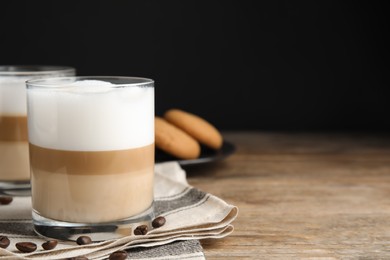 Delicious latte macchiato and coffee beans on wooden table, space for text