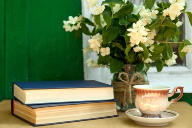 Books, cup of aromatic drink and beautiful jasmine flowers on wooden table near window outdoors