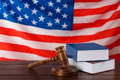 Judge's gavel and books on wooden table against American flag, space for text