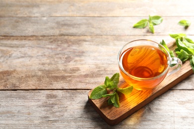 Cup with hot aromatic mint tea and fresh leaves on wooden board