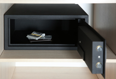 Open steel safe with money and smartphone in wooden closet