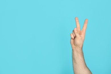 Young man showing victory gesture on color background. Space for text