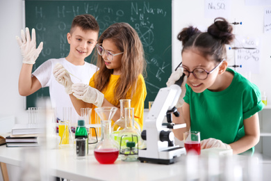 Schoolgirl looking through microscope and her classmates at chemistry class