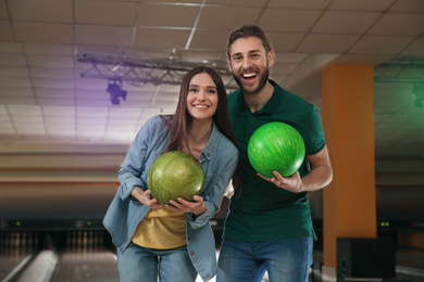 Happy young couple with balls in bowling club