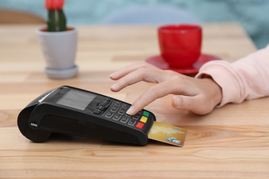 Woman using card machine for non cash payment at table, closeup