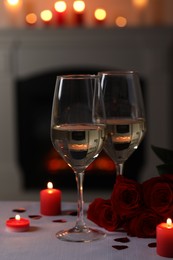 Photo of Glasses of white wine, rose flowers and burning candles on grey table indoors. Romantic atmosphere