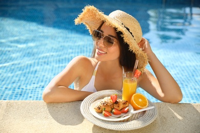 Photo of Young woman with delicious breakfast on tray in swimming pool